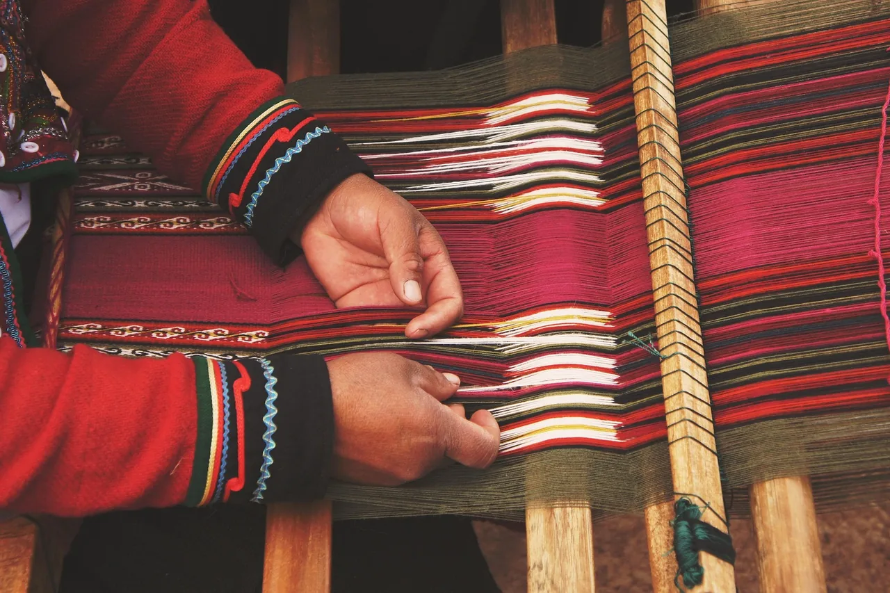 A weaver's hands working coloured threads on a traditional handloom